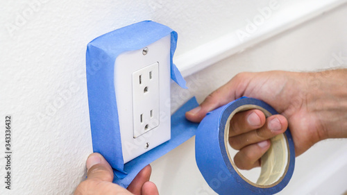 Painter Man Using Masking Blue Tape to Secure Electric Outlet.