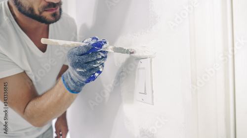 Close up of painter hands with gloves painting the wall edge with brush.
