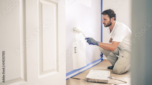 Painter man painting the wall in home, with paint roller and white color paint.