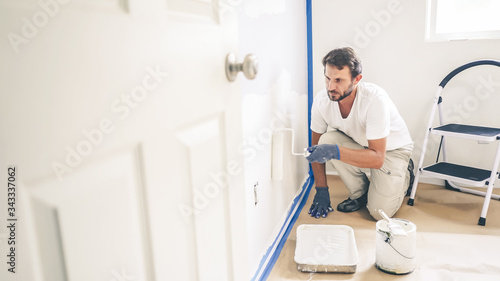 Painter man painting the wall in home, with paint roller and white color paint.