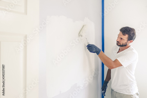 Painter man painting the wall in home, with paint roller and white color paint.