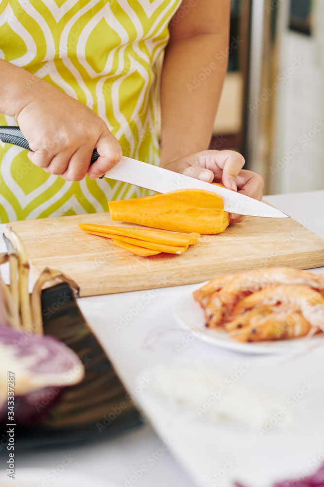 Housewife cutting carrot in thin slices with sharp knife when cooking dinner