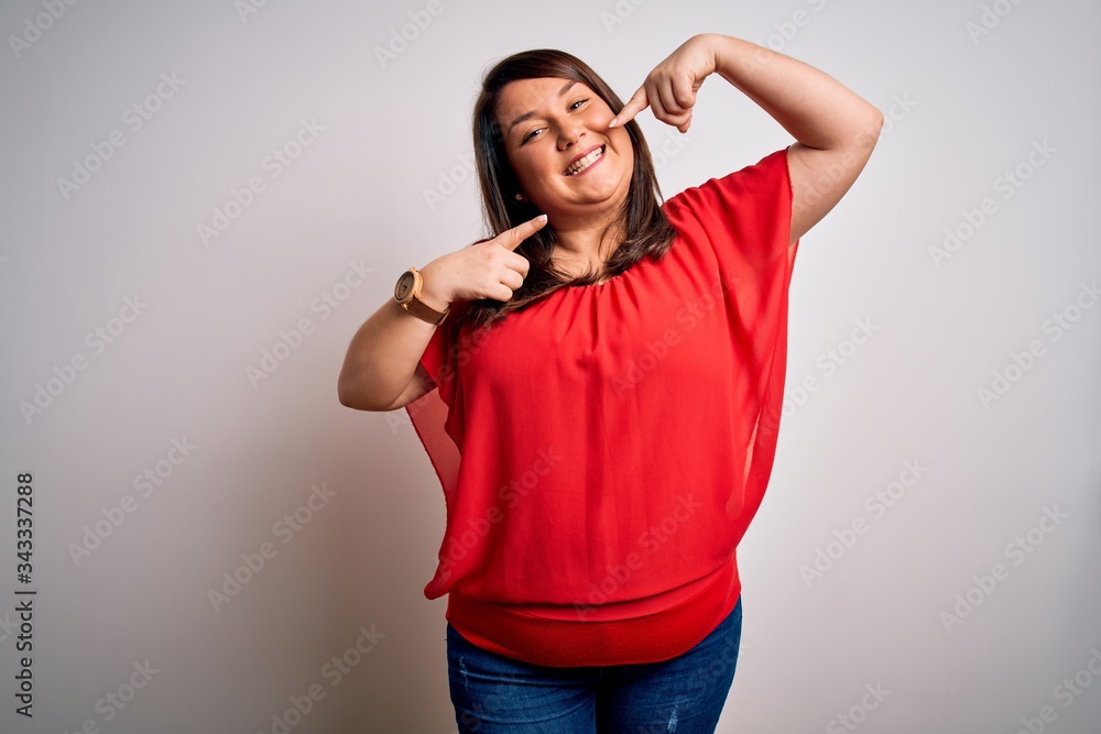 Beautiful brunette plus size woman wearing casual red t-shirt over isolated white background smiling cheerful showing and pointing with fingers teeth and mouth. Dental health concept. Beautiful brunette plus size woman wearing casual red t-shirt over isolated white background smiling cheerful showing and pointing with fingers teeth and mouth. Dental health concept.