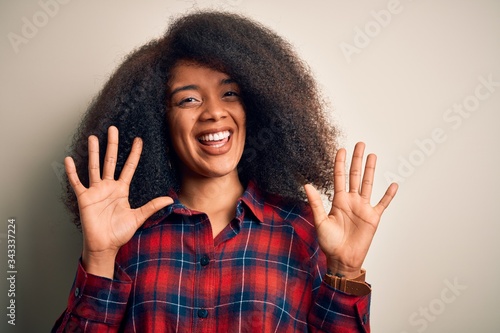 Young beautiful african american woman wearing casual shirt over isolated background showing and pointing up with fingers number ten while smiling confident and happy. © Krakenimages.com