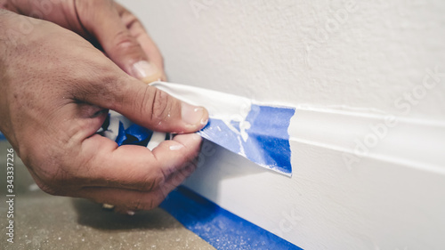 Painter Man Removing masking blue tape from molding, baseboard.
