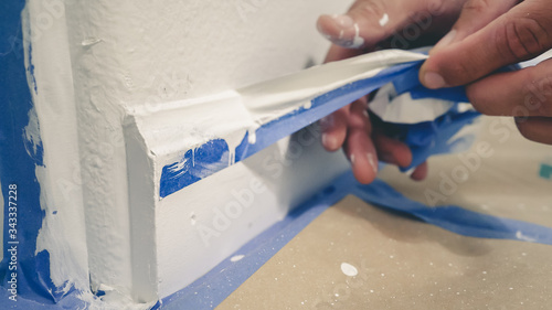 Painter Man Removing masking blue tape from molding, baseboard.