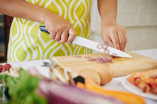 Housewife in apron cutting lotus stem in thin slices when cooking dinner photo