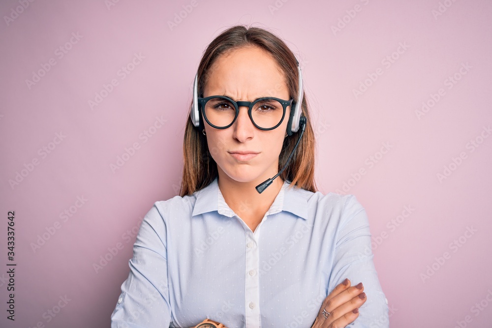 Young beautiful call center agent woman wearing glasses working using headset skeptic and nervous, disapproving expression on face with crossed arms. Negative person.