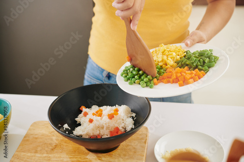 Woman cokking at home during covid19 quarantine and adding vegetables in bowl with boiled rice photo