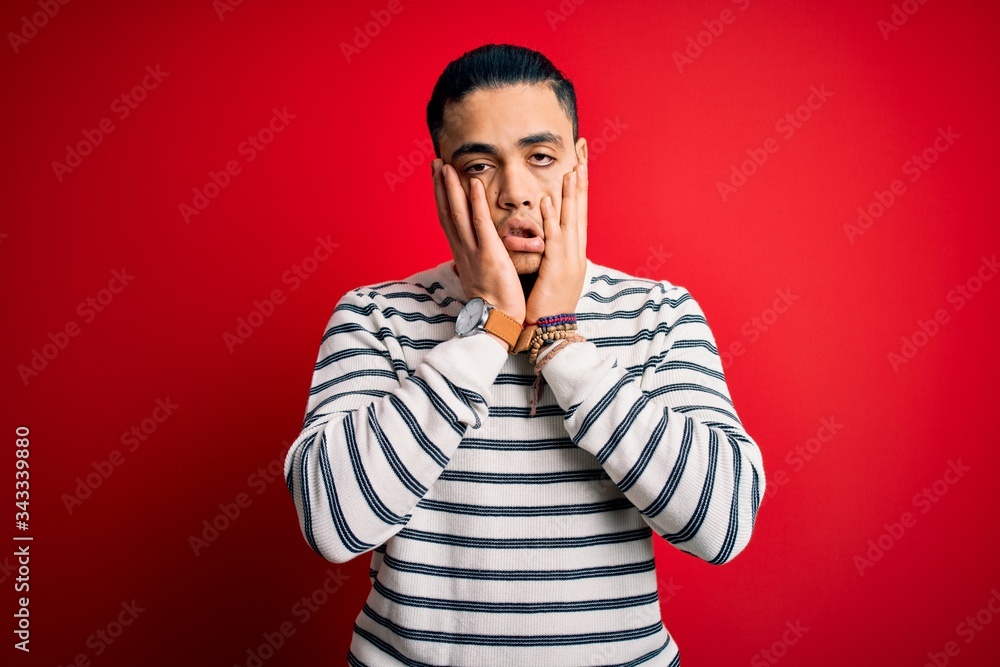 Young brazilian man wearing casual striped t-shirt standing over isolated red background Tired hands covering face, depression and sadness, upset and irritated for problem Young brazilian man wearing casual striped t-shirt standing over isolated red background Tired hands covering face, depression and sadness, upset and irritated for problem