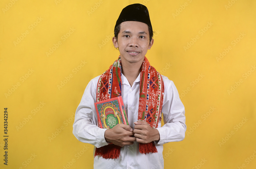 A man holds the Quran in his hand with a yellow background
