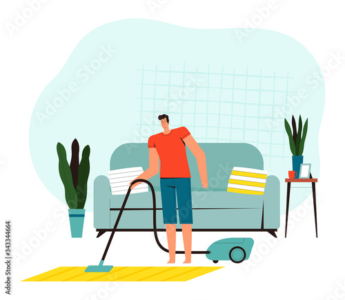Young man vacuums a carpet in front of a sofa at home. Concept of house cleaning on self-isolation. People doing home everyday activities