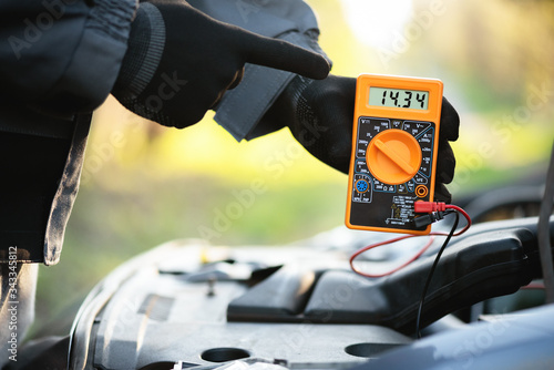 Fotografía Worker with multimeter near open car hood. Auto electrician.