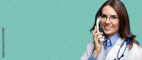 Portrait picture of happy smiling young doctor talking on phone, green marine background. Copy space for some sign, slogan or advertising text. Medical call center service. photo