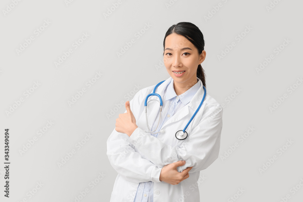 Female Asian doctor showing thumb-up on light background Female Asian doctor showing thumb-up on light background