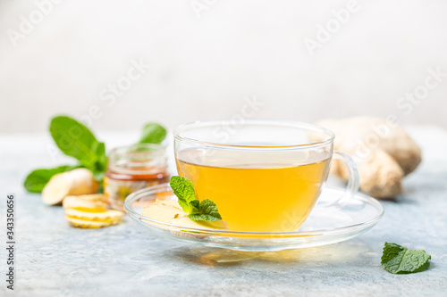 Ginger tea in a glass cup with lemon and mint on light background