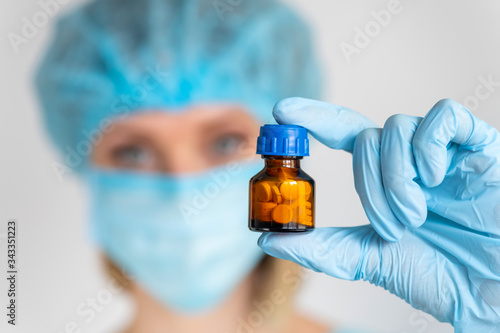 Young attractive female hurse or doctor with gloves and mask holding a pill in hand