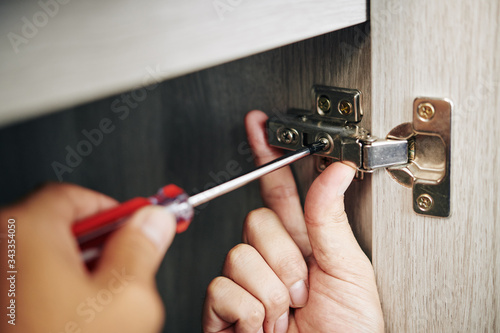 Wallpaper Mural Close-up image of handyman assembling kitchen cabinet and screwing door hinge