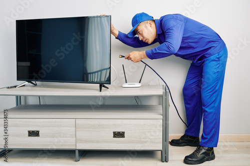Serious young Vietnamese repairman installing tv set in apartment of customer