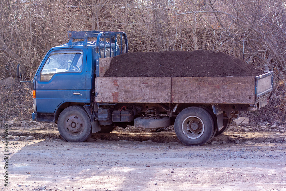 An old truck with a large pile of soil in the back. Soil delivery to order. Blue cabin. Horizontal.