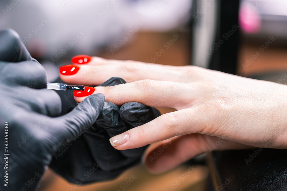 Close Up of master in rubber gloves covering red nails with top coat in the beauty salon. Perfect nails manicure process. Gel polish concept.