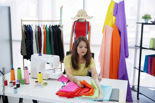 Asian senior woman designer is sitting and choosing the fabric pattern at workshop studio