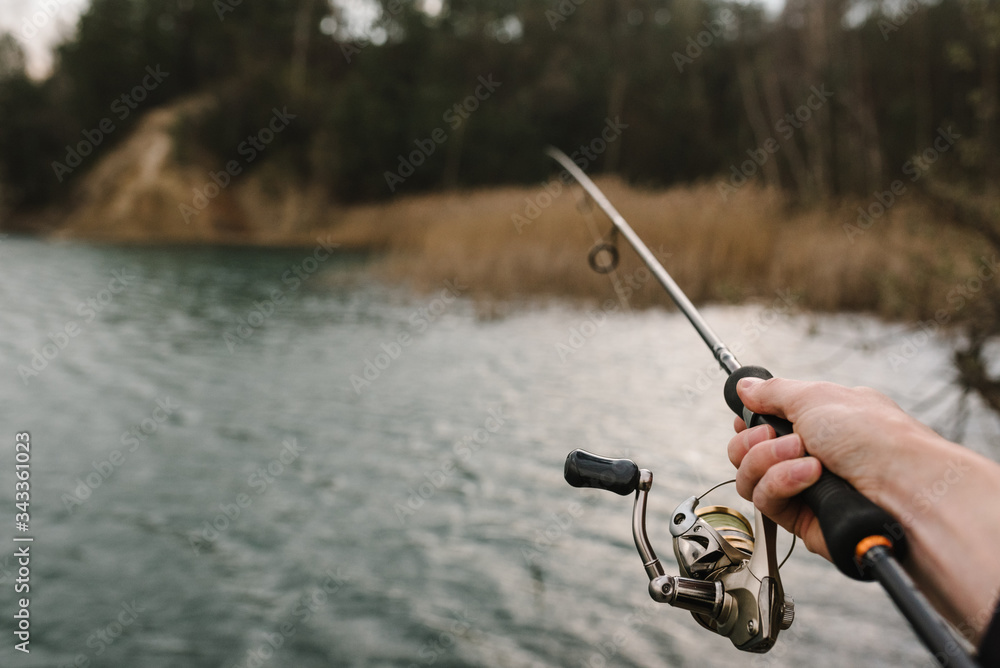 Fisherman with rod, spinning reel on the river bank. Man catching fish,  pulling rod while fishing
