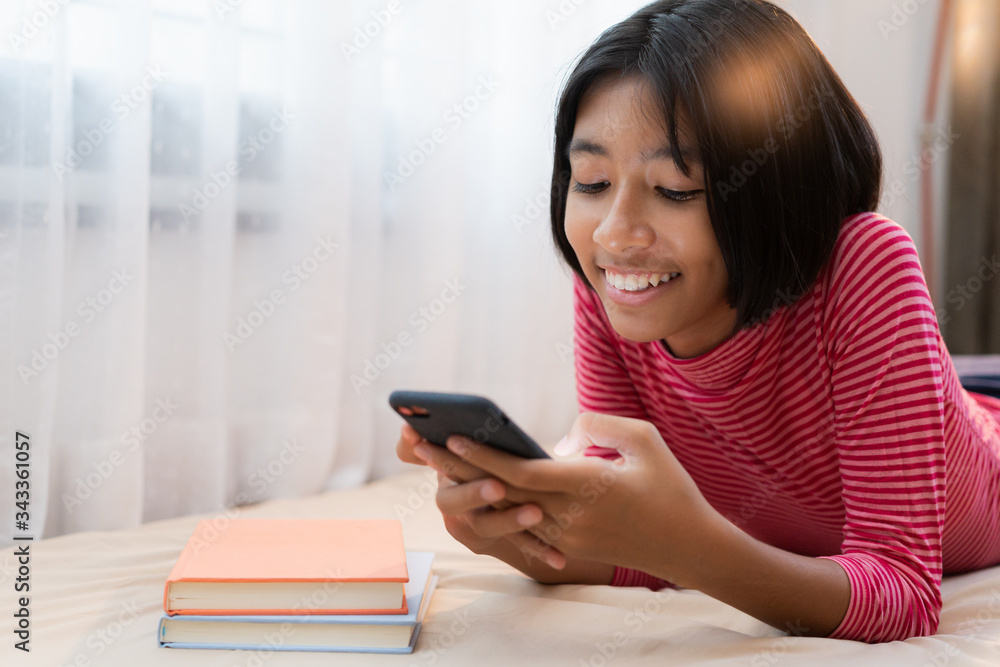 Happy Asian girl using the smartphone while lying in the bedroom at home night, Asia child smile and enjoy the laugh expression on the face. Concept relax and lifestyle at home Happy Asian girl using the smartphone while lying in the bedroom at home night, Asia child smile and enjoy the laugh expression on the face. Concept relax and lifestyle at home
