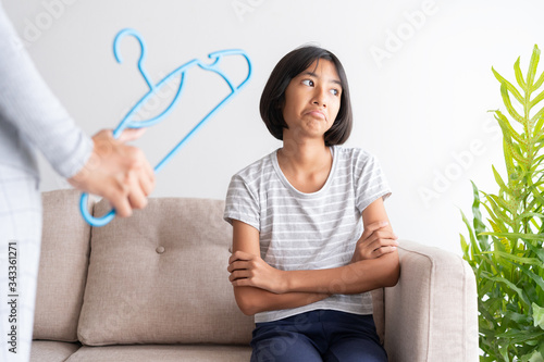 Slika na platnu Mother is punishing her daughter by hitting with a hanger while sitting on the sofa because of bad behavior