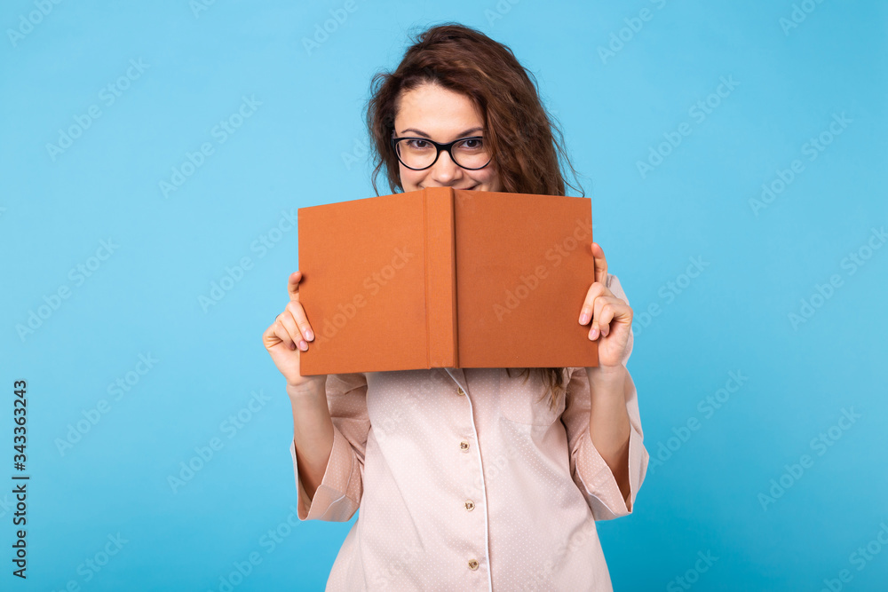 Young girl is reading a book in pajamas on blue background. Relax good mood, lifestyle and sleepwear concept. Young girl is reading a book in pajamas on blue background. Relax good mood, lifestyle and sleepwear concept.