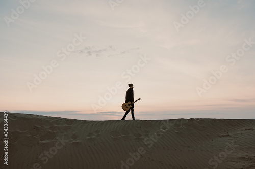 long haired musician with guitar walking on a hill in the sunset