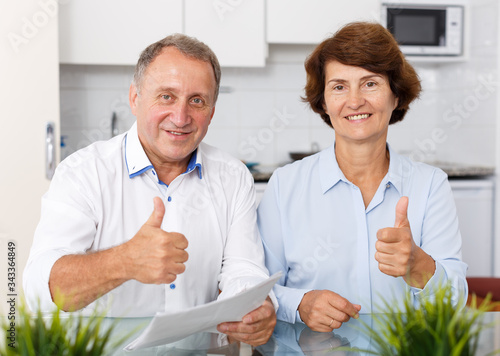 Positive mature couple sitting  with documents and holding thums up photo