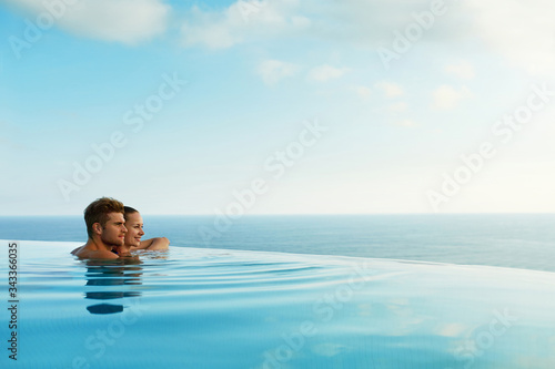 Couple In Love At Luxury Resort On Romantic Summer Vacation. People Relaxing Together In Edge Swimming Pool Water, Enjoying Beautiful Sea View. Happy Lovers On Honeymoon Travel. Relationship, Romance