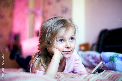 A beautiful girl lies on a bed with a phone and dreams of something. Dreamy facial expression. Close-up of the face, the face rests on the hand.