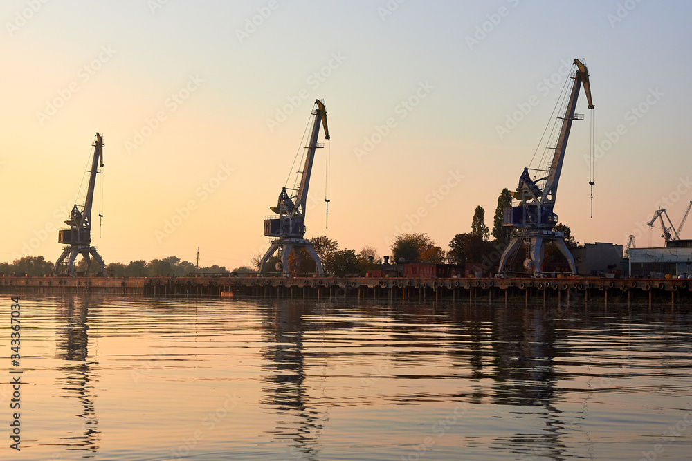 Port cranes, harbour cranes on the river bank at sunset Port cranes, harbour cranes on the river bank at sunset
