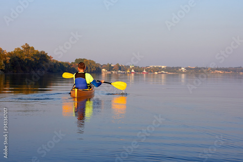 Kayaking in the Danube river at sunset at calm early autumn day. Man paddle at the yellow kayak