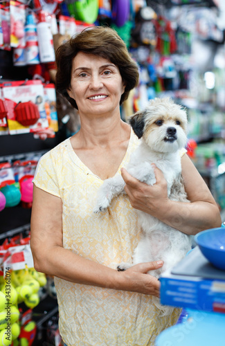 Portrait of happy elderly woman visiting pet supplies store with her cute puppy of havanese