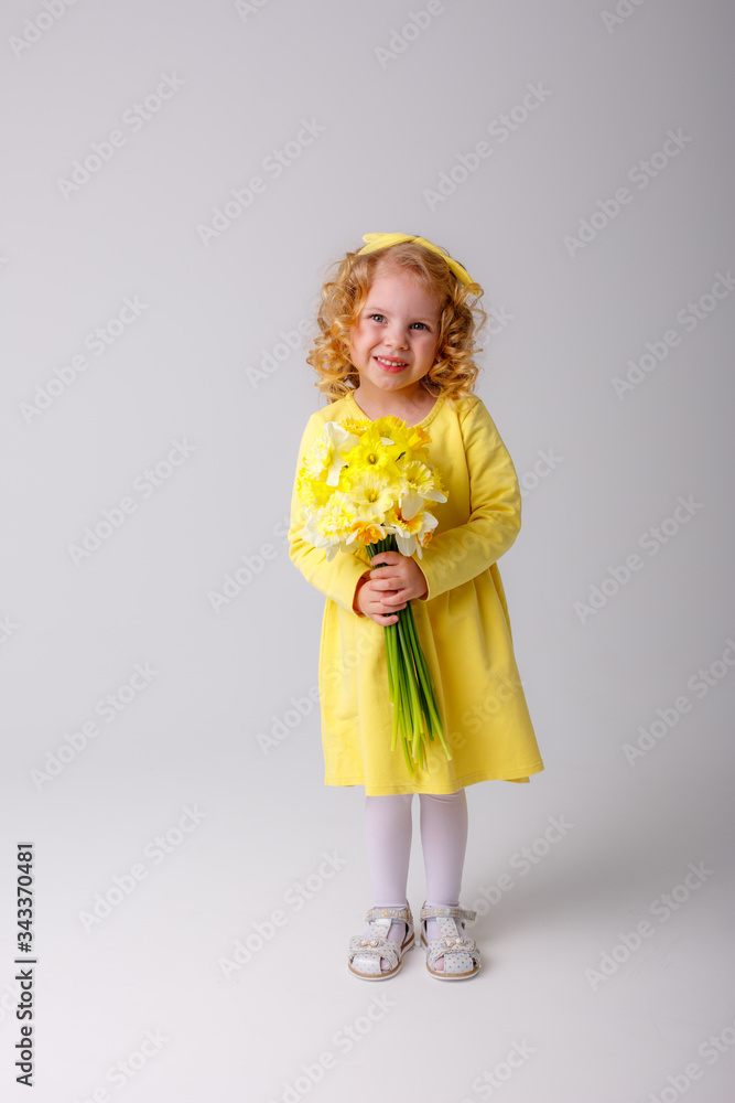 a small curly haired girl in a yellow dress holding a bouquet of spring flowers on a white background smiles a small curly haired girl in a yellow dress holding a bouquet of spring flowers on a white background smiles