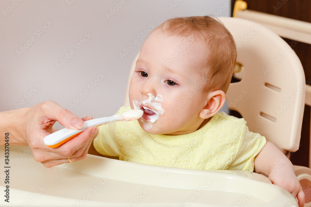feeding the baby with a spoonful of baby curd. the child sits in a child's chair for feeding and eats. feeding the baby with a spoonful of baby curd. the child sits in a child's chair for feeding and eats.
