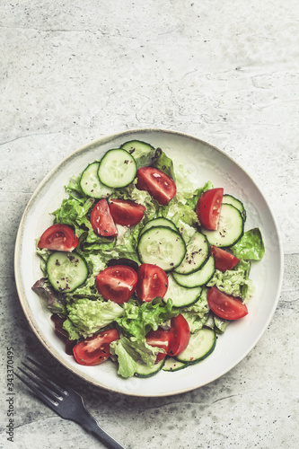 Fresh tomato and cucumber salad in white bowl, gray background. Healthy food concept.