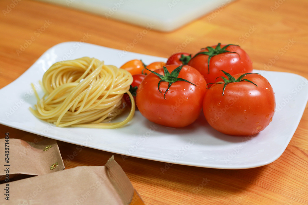 Raw pasta noodles with fresh tomatoes on a white plate. Fresh spaghetti ingredients on the wooden table. Raw pasta noodles with fresh tomatoes on a white plate. Fresh spaghetti ingredients on the wooden table.
