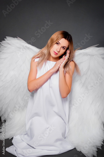 Young woman in a white dress with white wings behind her back. Girl in the image of an angel isolated on a gray background.