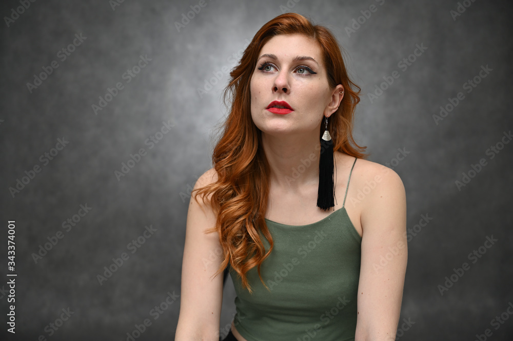Portrait on a gray background of a pretty red-haired young woman. A model with great makeup posing in a green t-shirt in the studio. Portrait on a gray background of a pretty red-haired young woman. A model with great makeup posing in a green t-shirt in the studio.