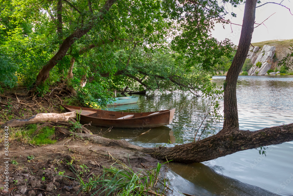 A beautiful landscape with old metal fishing boats near a riverbank under trees
