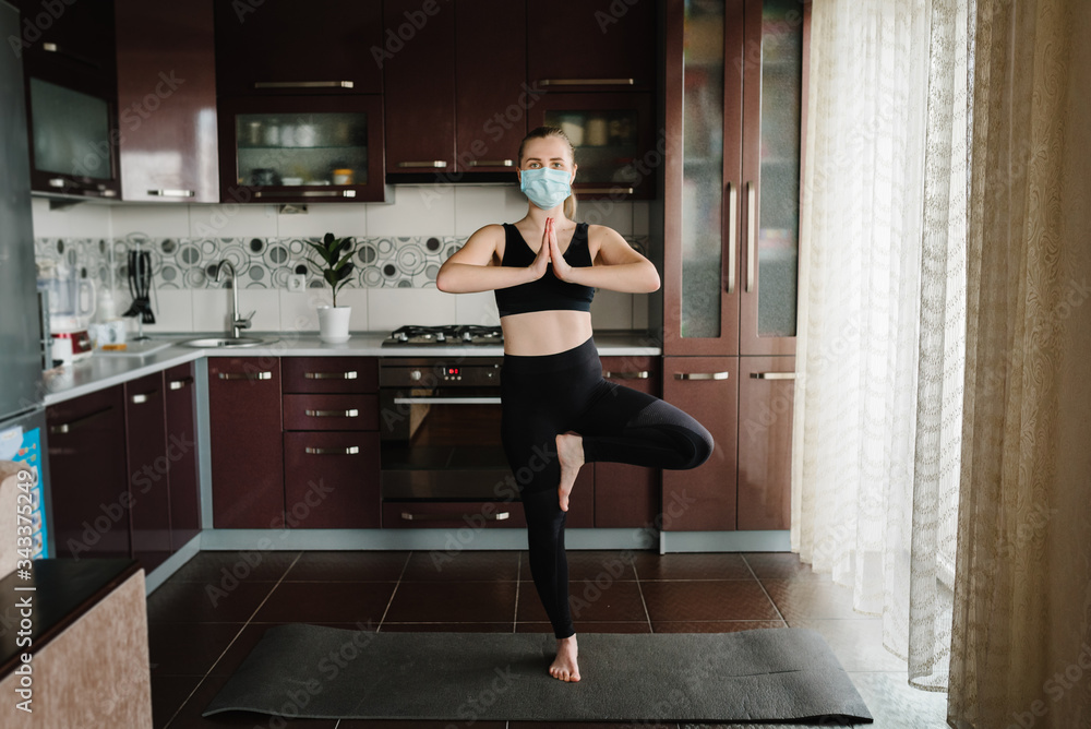 Girl in protective mask, sportswear on floor on mat at home. Woman are practicing yoga at home. Female doing morning work-out. Coronavirus. Stay Home. Sport at home. Calmness concept. Fitness workout. Girl in protective mask, sportswear on floor on mat at home. Woman are practicing yoga at home. Female doing morning work-out. Coronavirus. Stay Home. Sport at home. Calmness concept. Fitness workout.