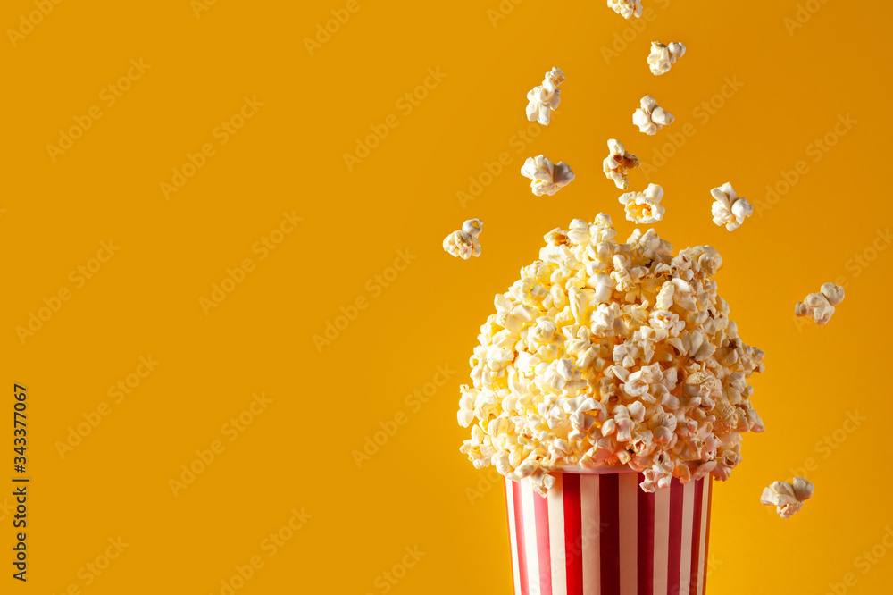 Paper striped bucket with popcorn on yellow background. Popcorn falling into the basket. Copy space.