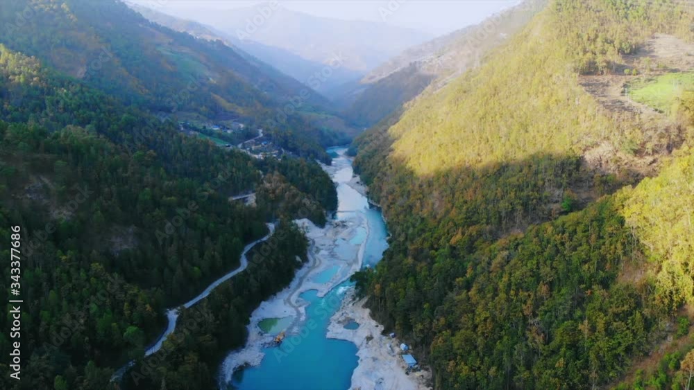 Drone shot of flying between a tight green valley river Tama koshi flowing between them during golden hour with road on the side. Aerial view on the way to Jiri, Dolakha. Developing nation Nepal 2019. Drone shot of flying between a tight green valley river Tama koshi flowing between them during golden hour with road on the side. Aerial view on the way to Jiri, Dolakha. Developing nation Nepal 2019.