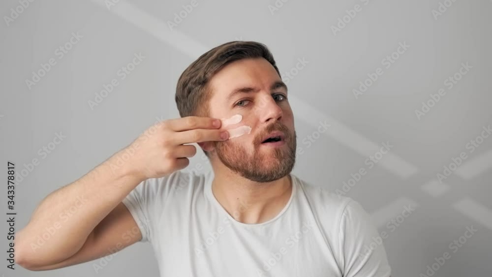 attractive man applies cream on face and smiles attractive man applies cream on face and smiles