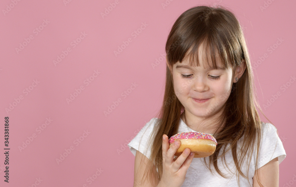 Studio portrait of a beautiful little girl holding a donut and smelling tasty flavour