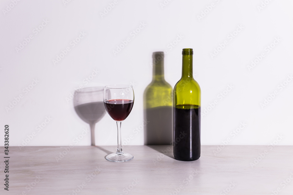 A glass of wine and a bottle casts a long shadow from the evening sun. A glass of wine and a bottle casts a long shadow from the evening sun.